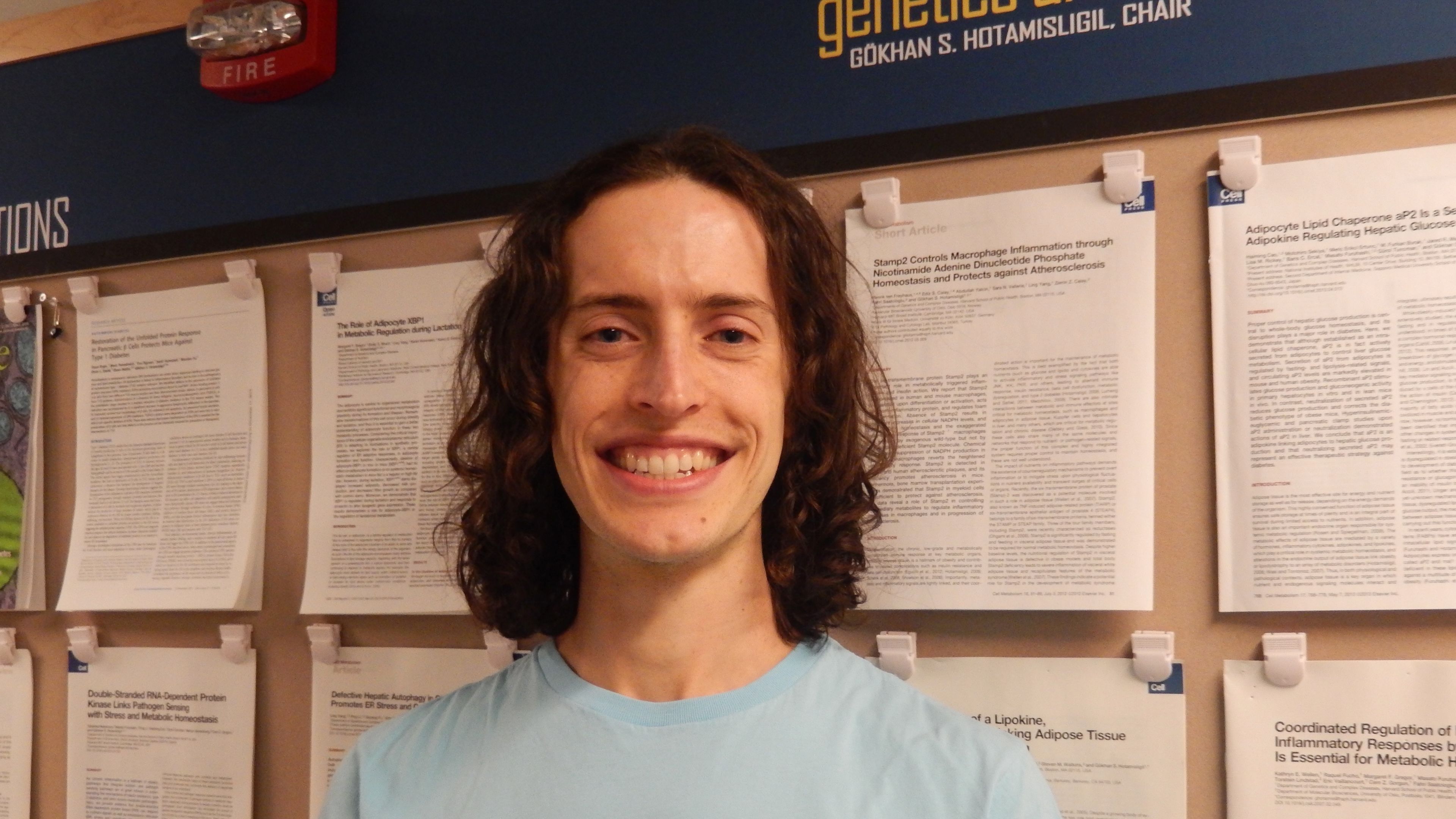 Brendon Smith in front of display of postdoc lab papers at Harvard